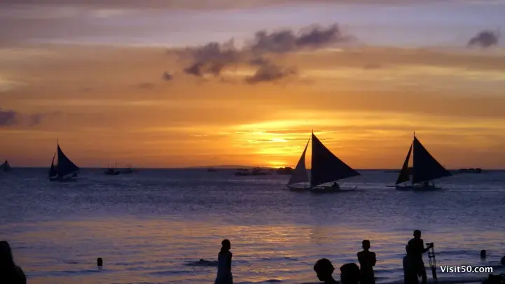 Sunset with orange purple and yellow with silhouettes of a sailboat and people on Boracay island in the Philippines