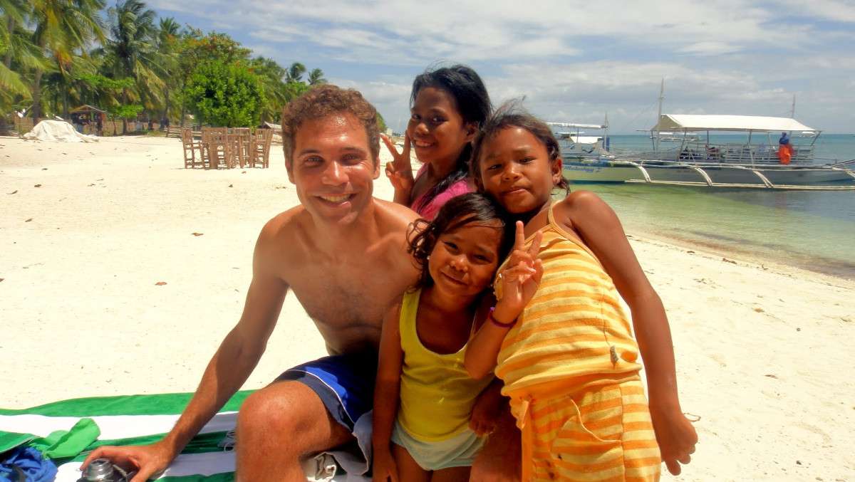 Visit50 founder Todd with three Filipino kids on the beach on Malapascua Island in the Philippines